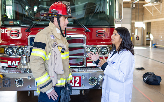 UC Davis researcher in lab coat speaking with firefighter in turnout gear at fire station