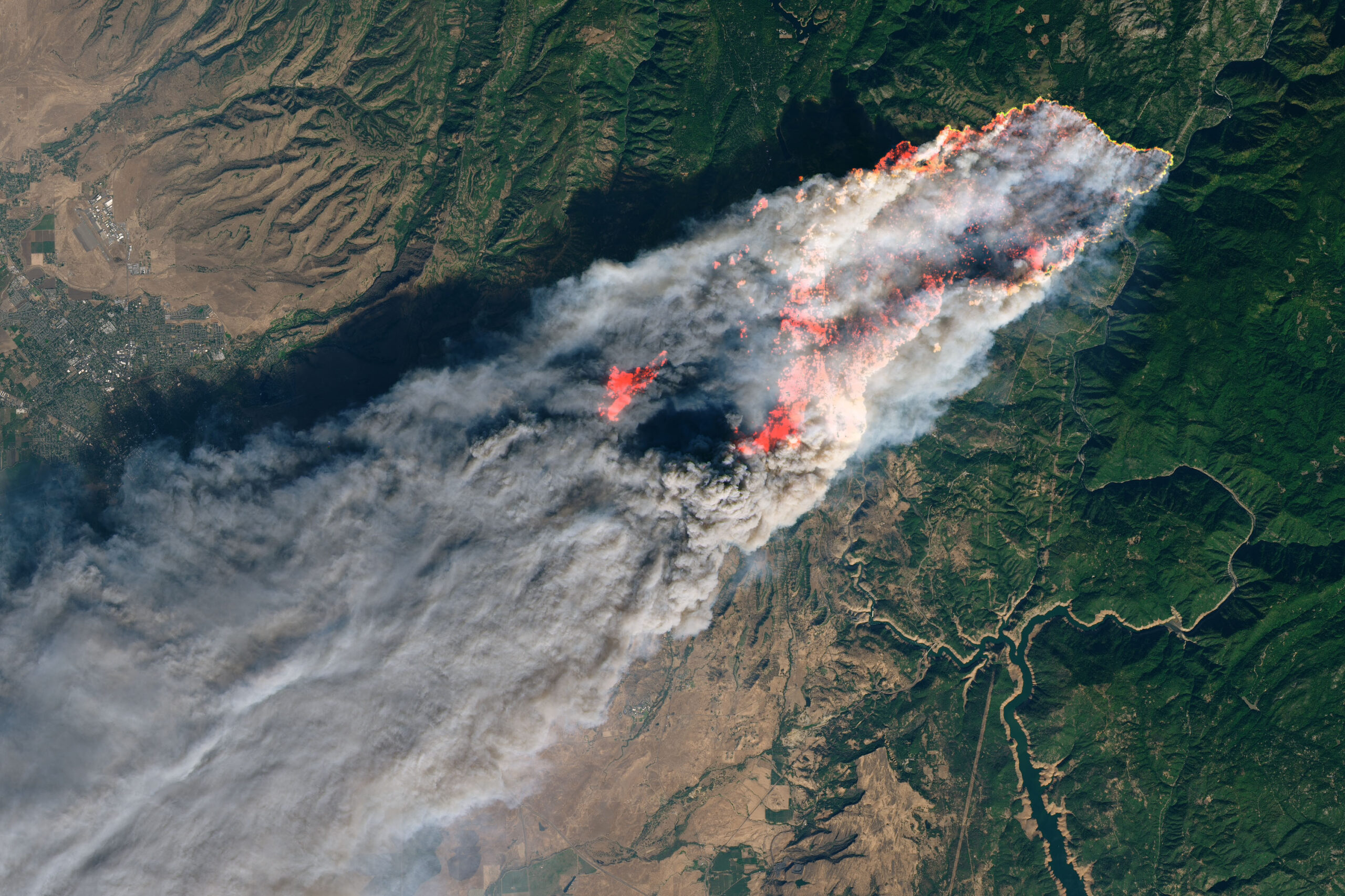 Satellite view of an active wildfire perimeter and smoke plume threatening a town