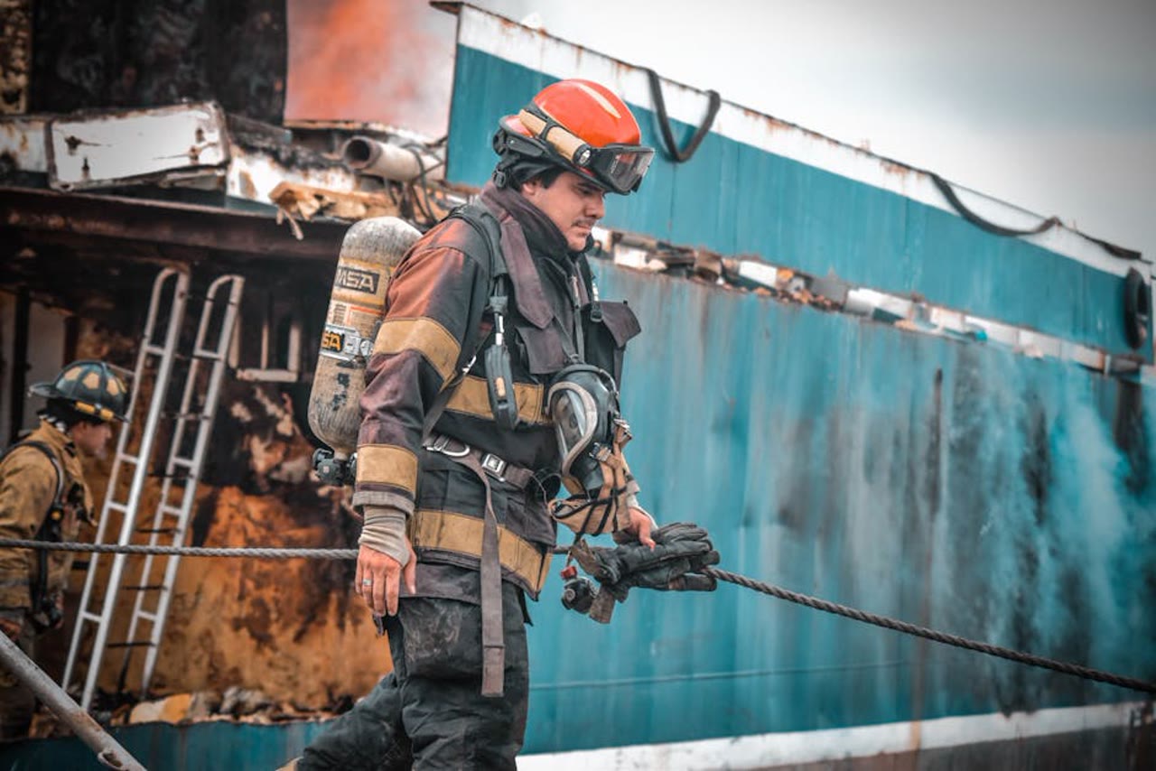 American firefighter in soot-streaked turnout gear, MSA SCBA, and red helmet at a fire scene