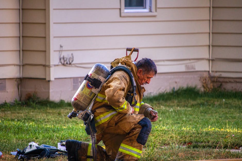 Firefighter in soot-stained turnouts and MSA SCBA kneeling on a suburban lawn after a structure fire