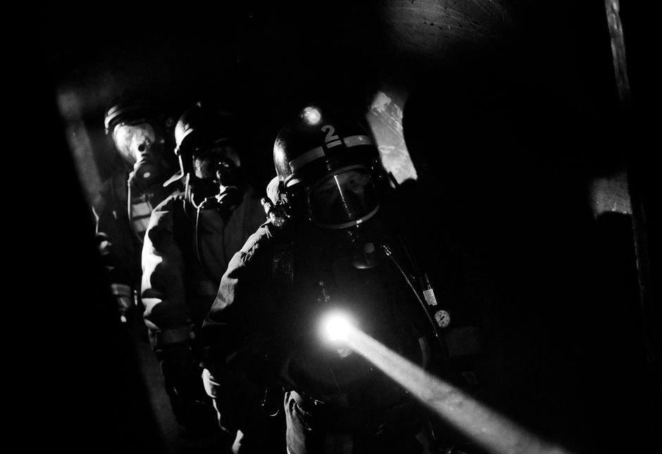 American firefighter crew advancing through dark smoke-filled interior with flashlight during search