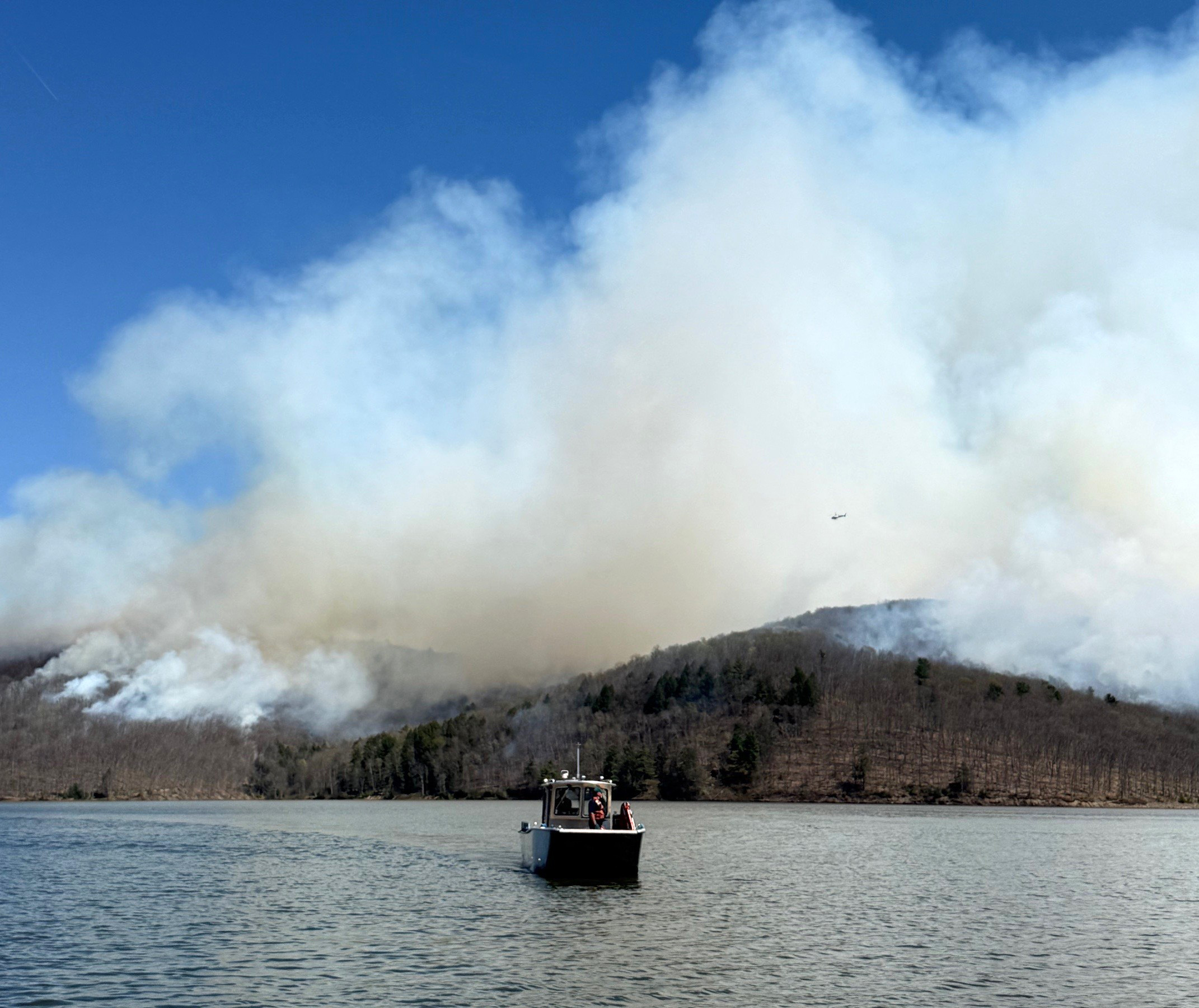 US Forest Service patrol boat on Allegheny Reservoir with a smoke column and helicopter overhead during prescribed fire operations