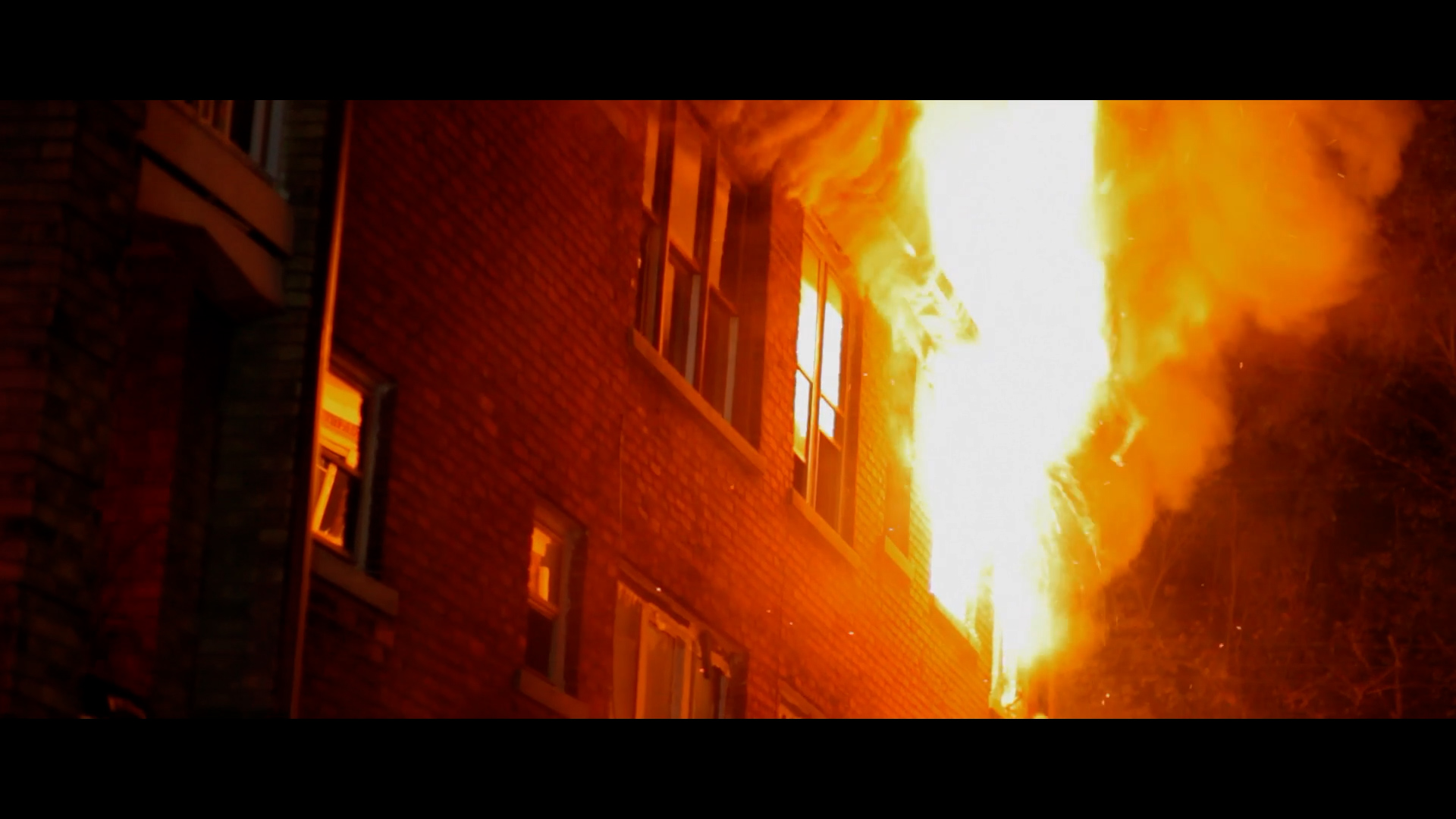 Tracked firefighting robot spraying water at a burning building in Ukraine at dusk