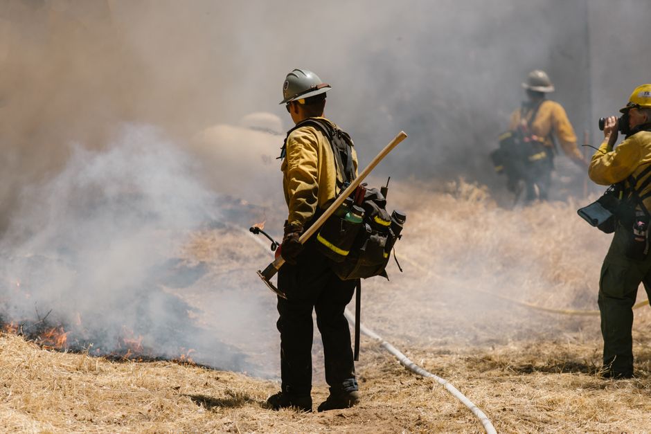 Firefighters combating a wildfire with heavy smoke and flames