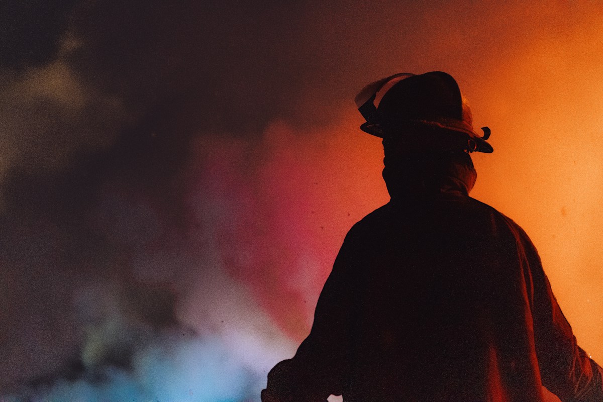 Firefighter silhouette with smoke and light, back to camera, helmet visible