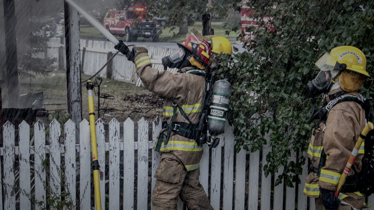 American firefighters operating a hose line in Chewelah, Washington; illustrative scene, not a test of the patented design